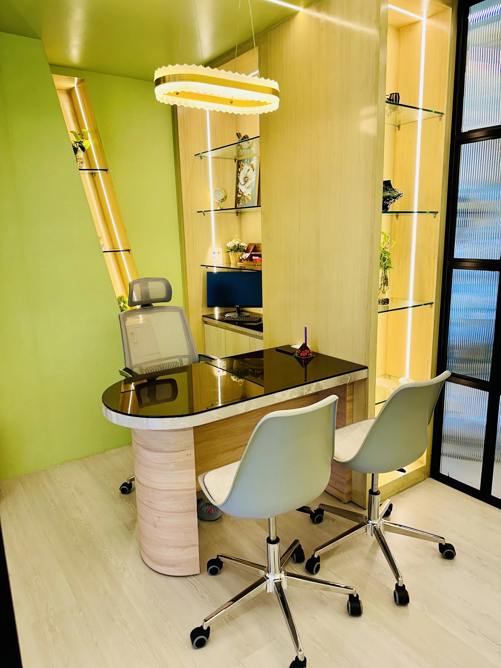 Consultation room at RH Dental Care Banani: a stone desk with two chairs facing it, beside backlit glass display shelves set into an oak slat wall.
