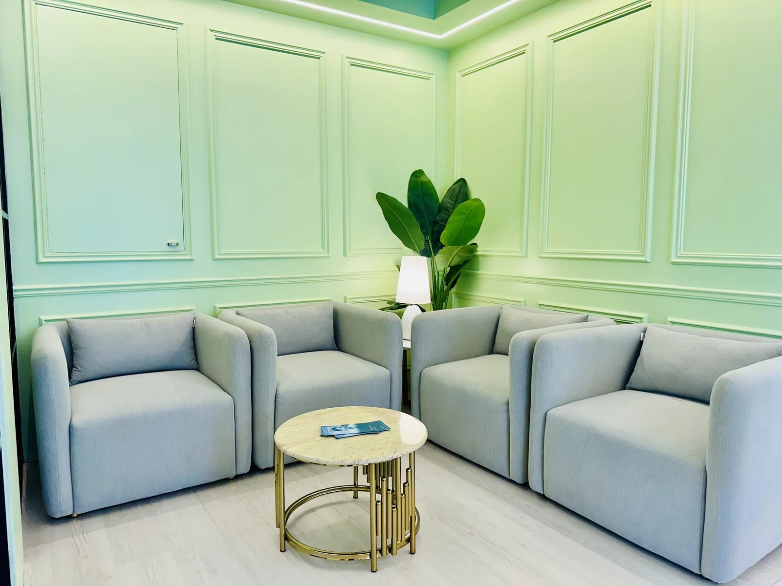 A panelled room at RH Dental Care Banani with four grey armchairs around a brass and marble table, lit by a cove strip running the ceiling perimeter.