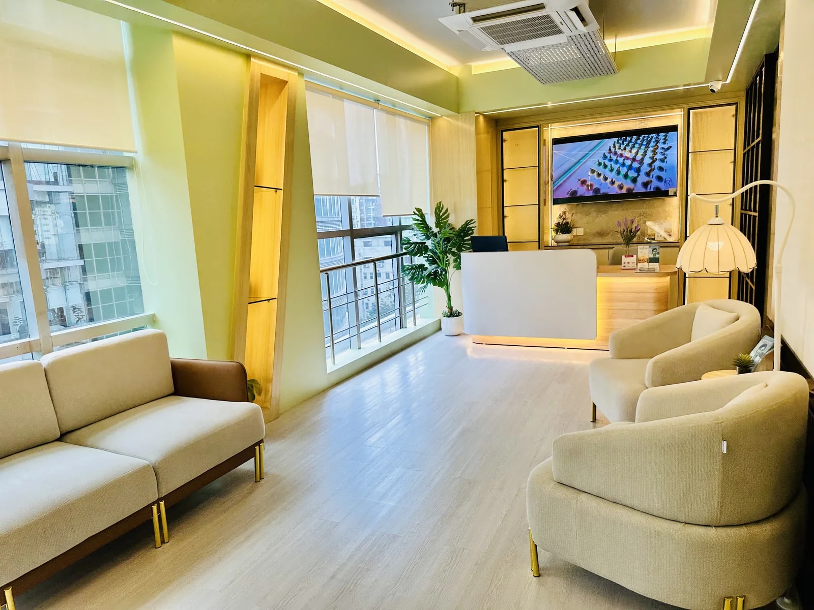 Reception at RH Dental Care Banani: a pale oak desk lit from beneath, cream seating, panelled sage-green walls and a full-height window looking out over Banani.