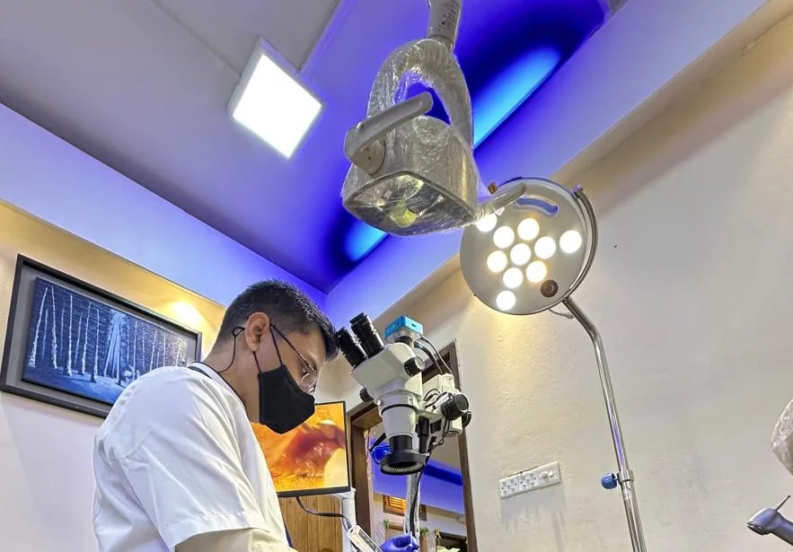 A clinician at an endodontic operating microscope at RH Dental Care Banasree, beneath the operating light.