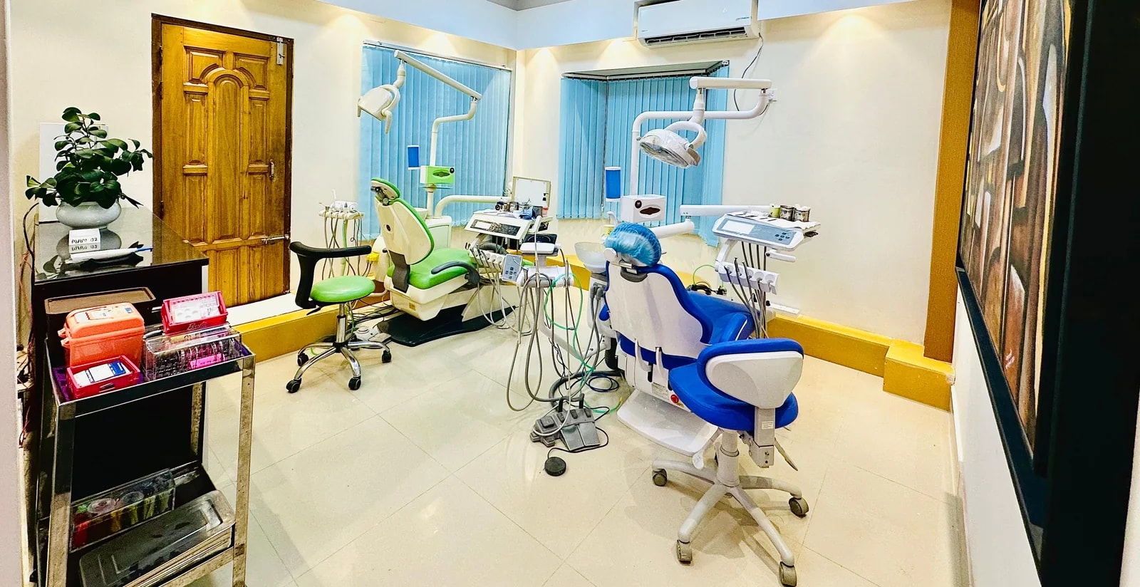 A treatment room at RH Dental Care Banasree with two dental chairs, instrument trolleys, overhead lights and a wall-mounted screen.