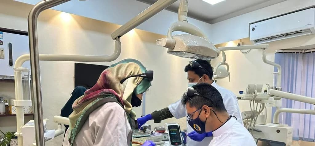 Three clinicians working together around a chair at RH Dental Care Banasree, with the operating light, a vitality monitor and the delivery unit around them.